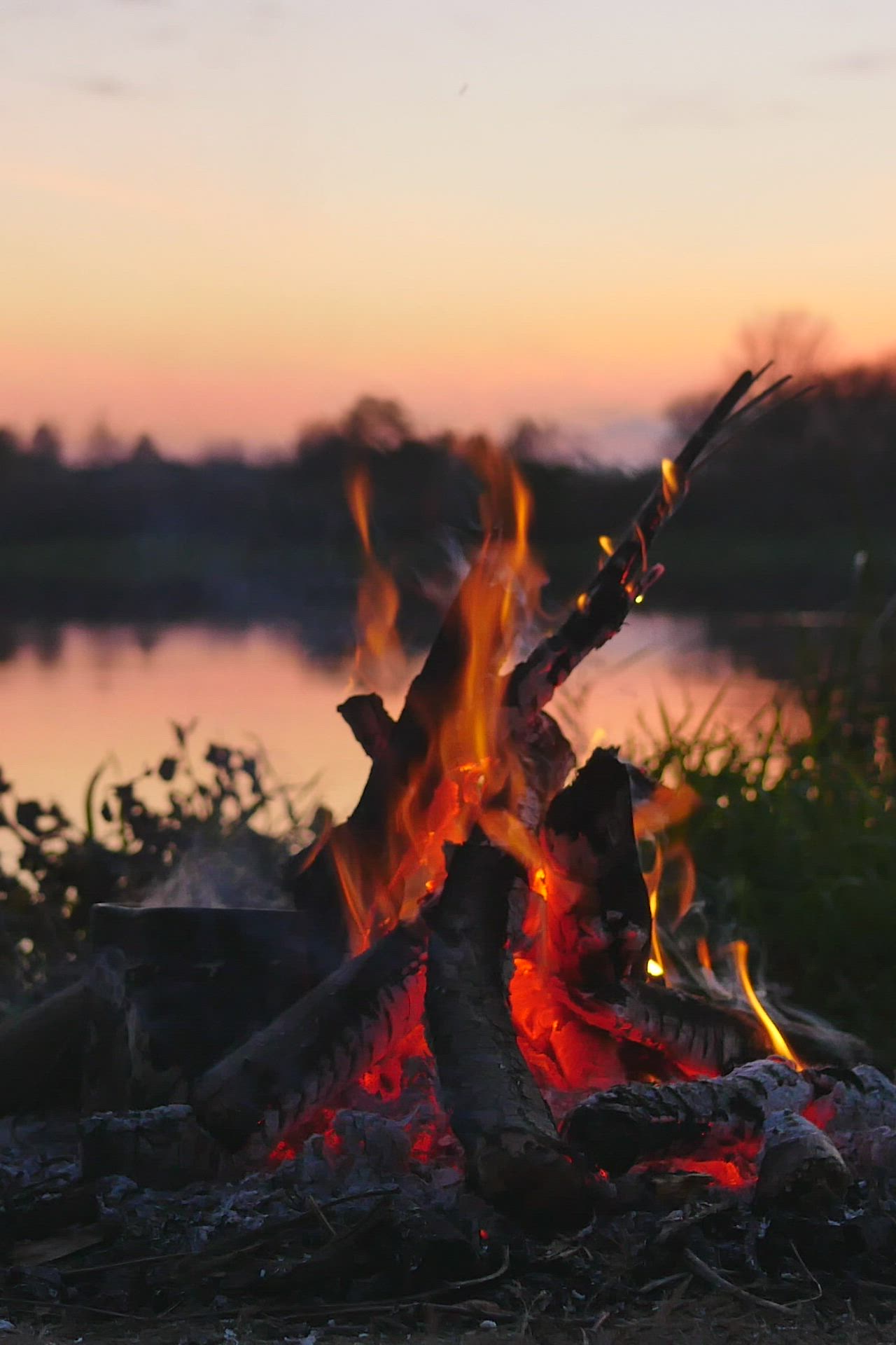 This may contain: a campfire is lit up by the water at sunset