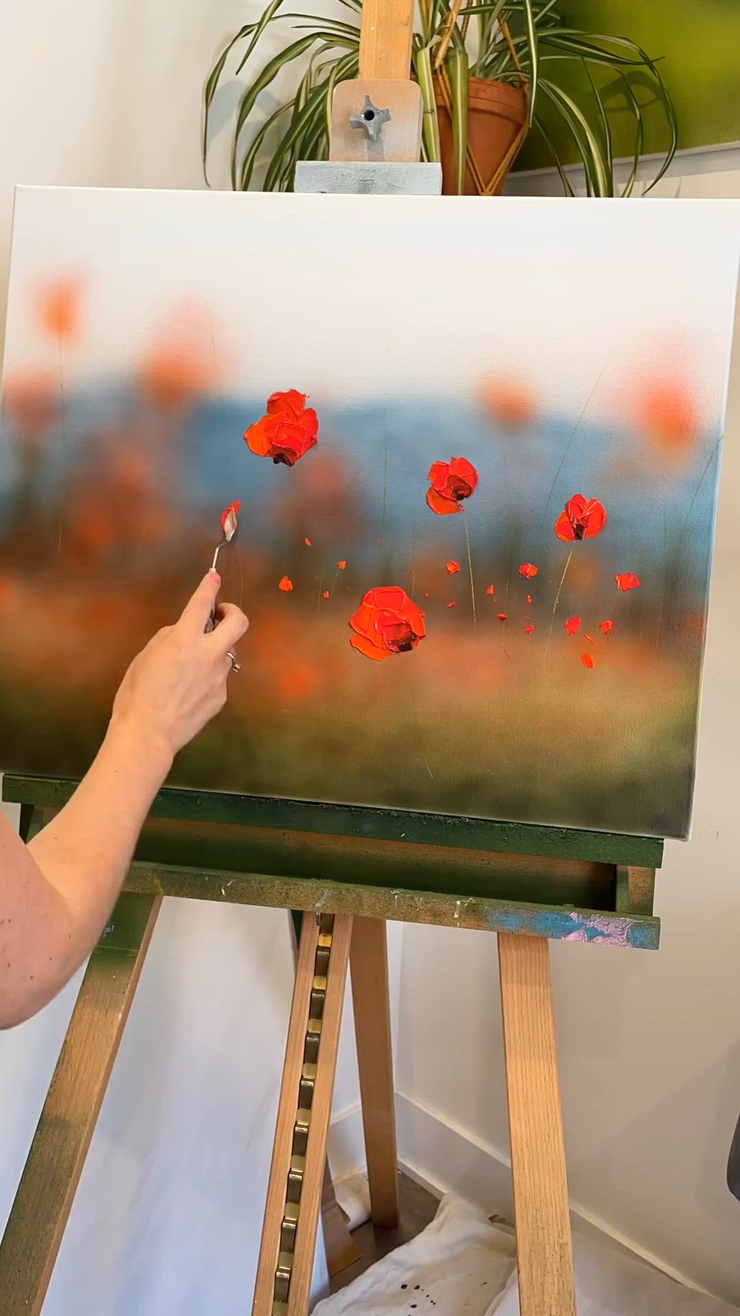 This may contain: a woman is painting red flowers on an easel