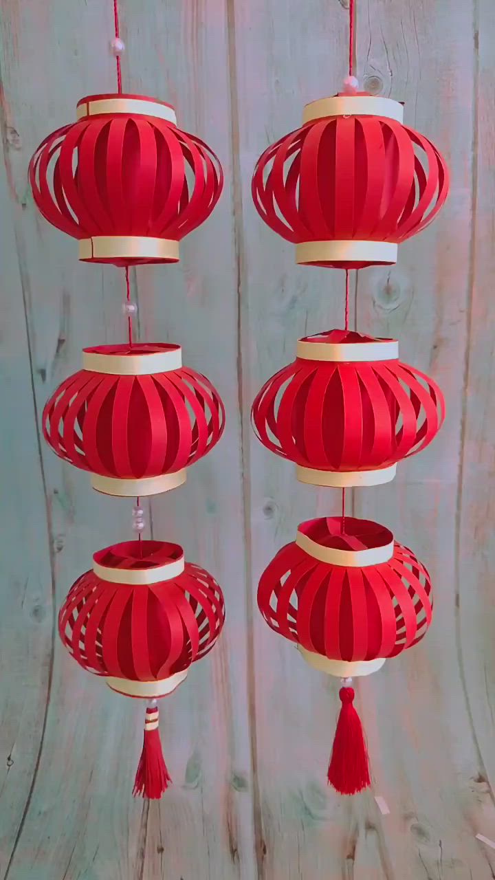 This may contain: three red lanterns with tassels hanging from them on a wooden surface, in the shape of chinese lanterns