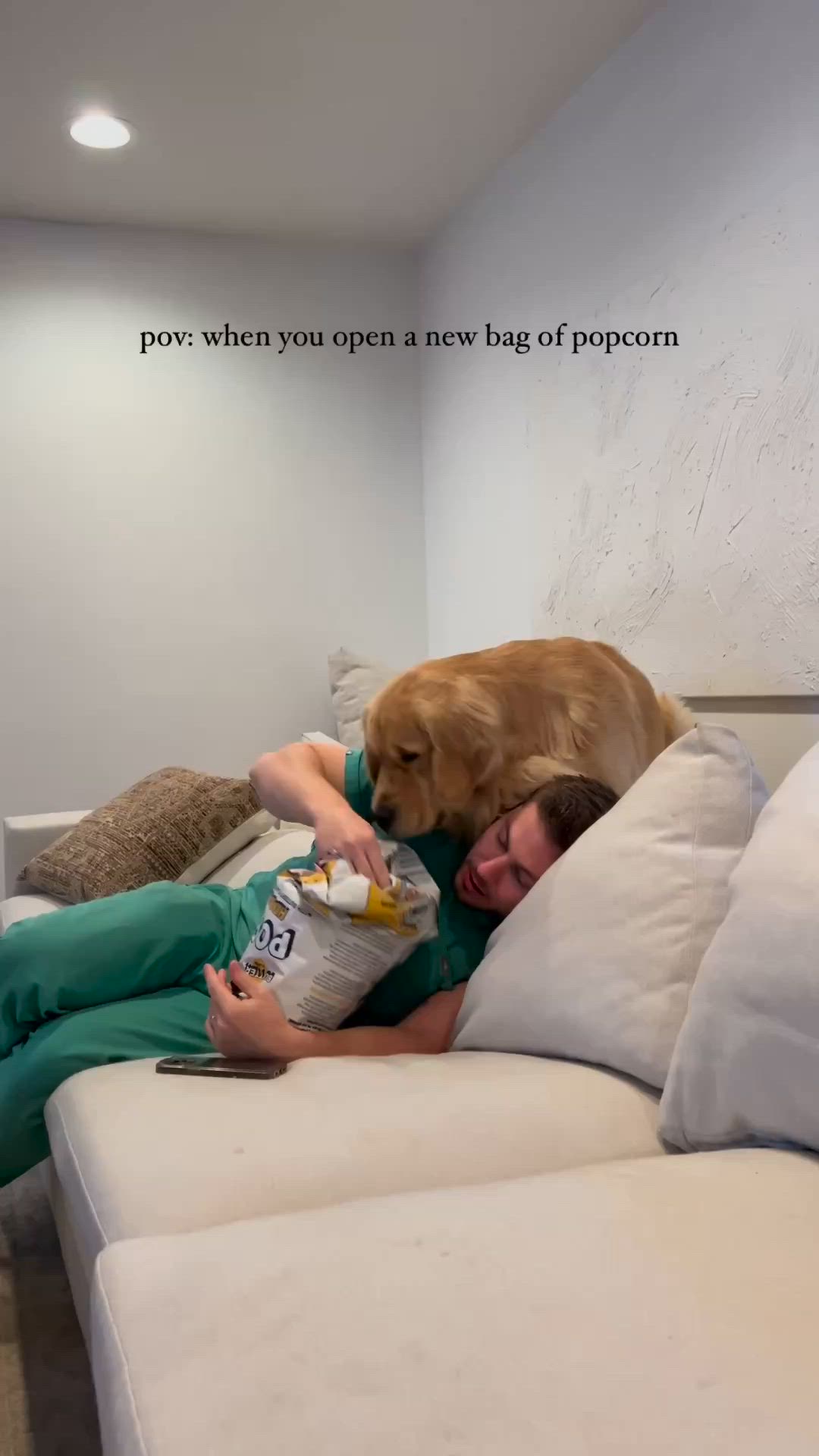 This may contain: a man laying on top of a white couch next to a dog with a bottle in it's mouth