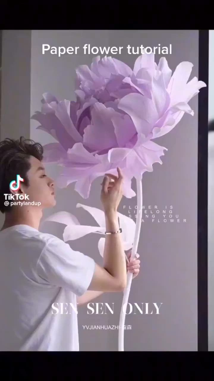 This may contain: a man holding a large purple flower in front of him with the words paper flower tutor on it