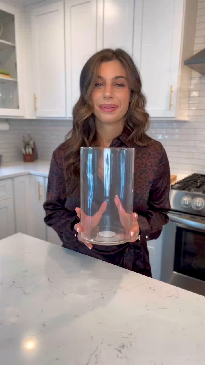 This may contain: a woman is holding a glass in her hands while standing at the kitchen counter top