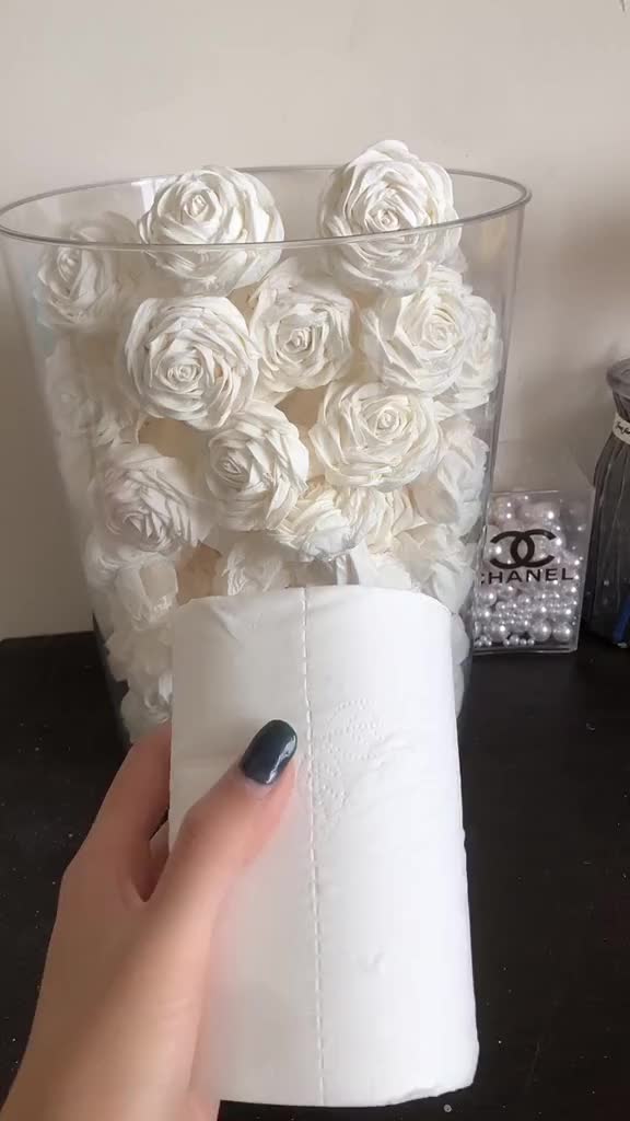 This may contain: a person holding a roll of toilet paper in front of a vase filled with white roses