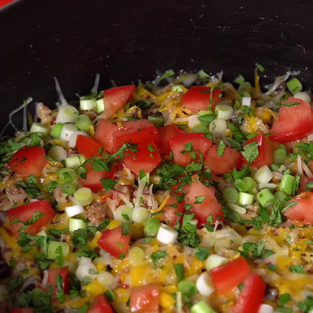 This may contain: a spoon scooping some food out of a skillet filled with rice and veggies