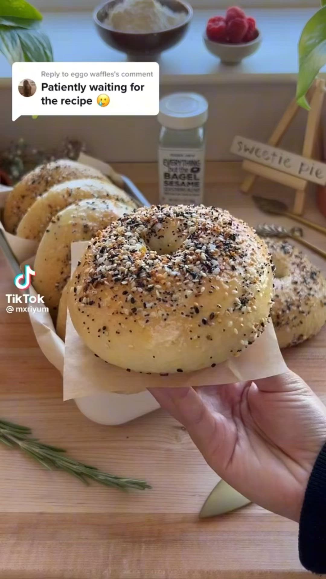 This may contain: a person holding a bagel in front of several other bagels on a cutting board
