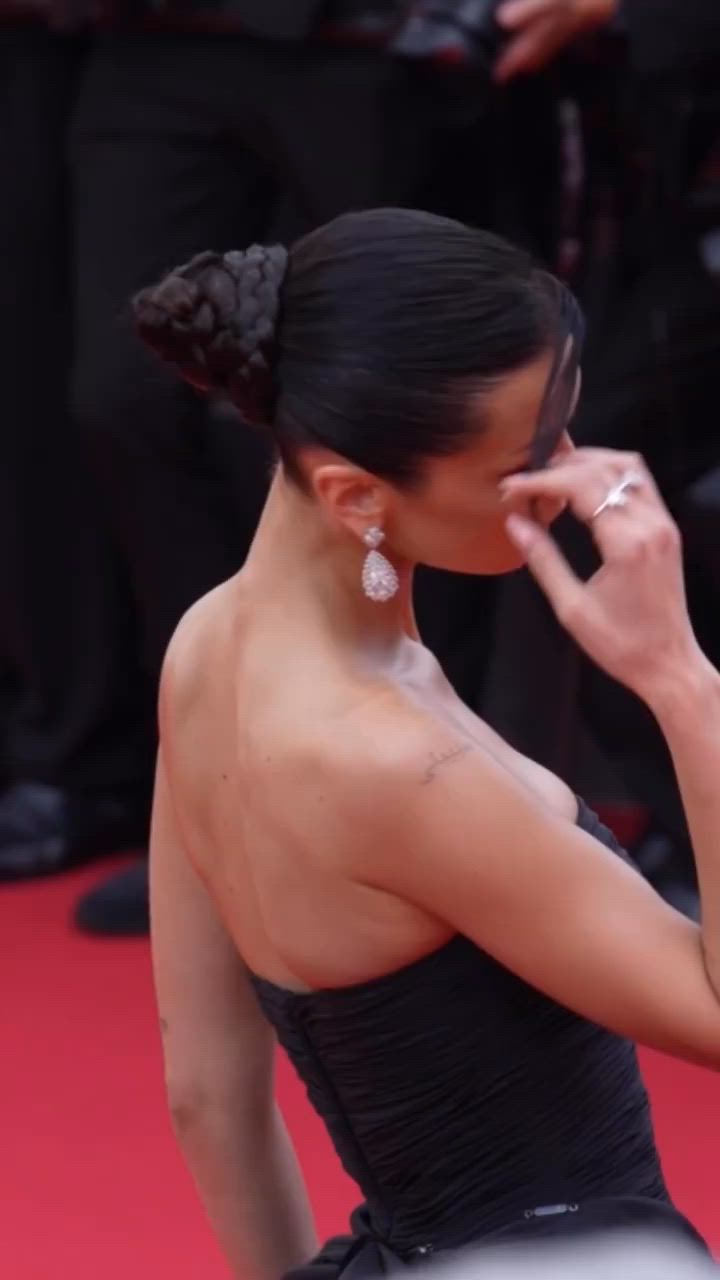 This may contain: a woman in a black dress standing on a red carpet with her hand near her face