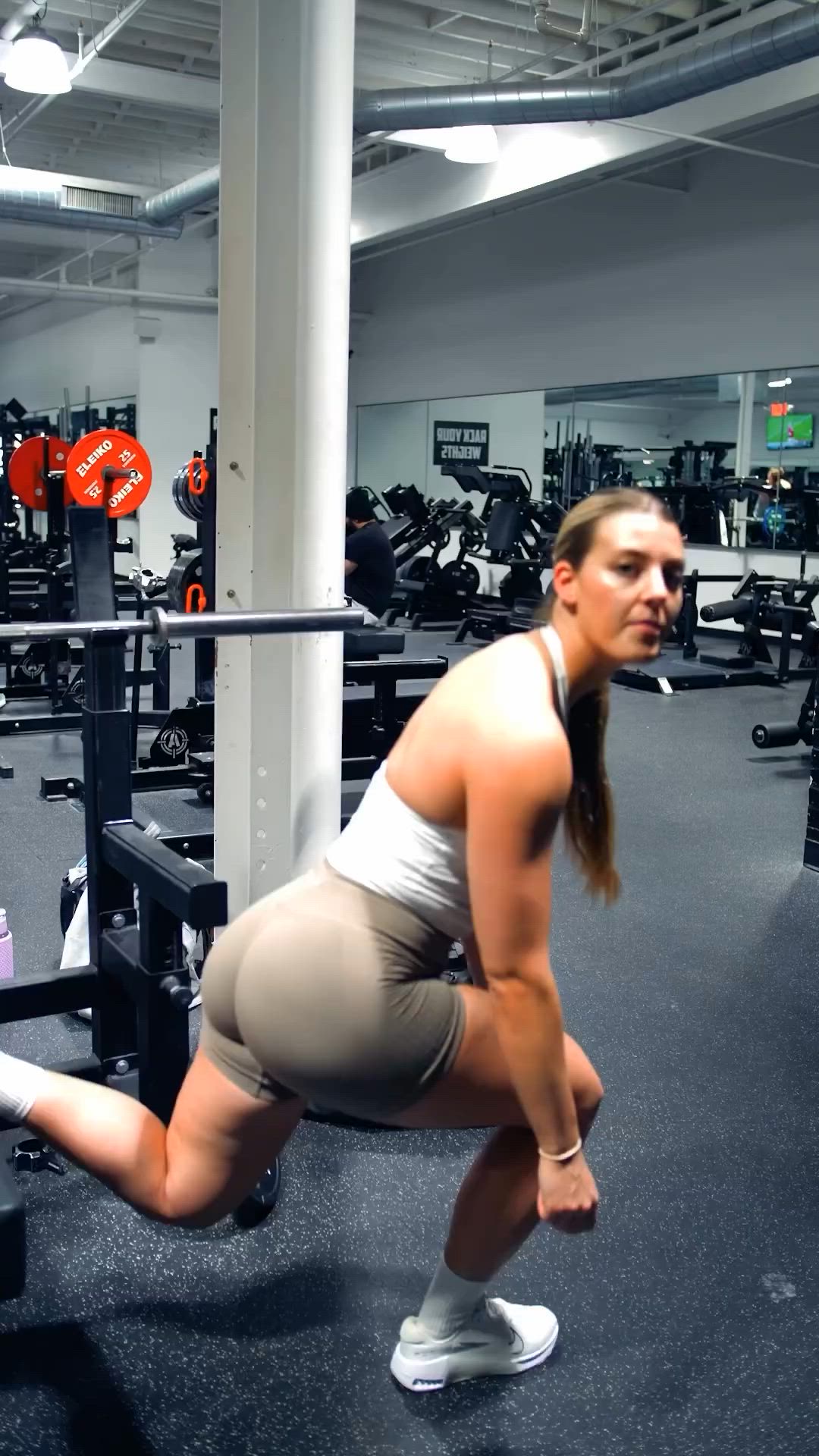 This may contain: a woman is standing in the middle of a gym with a barbell behind her