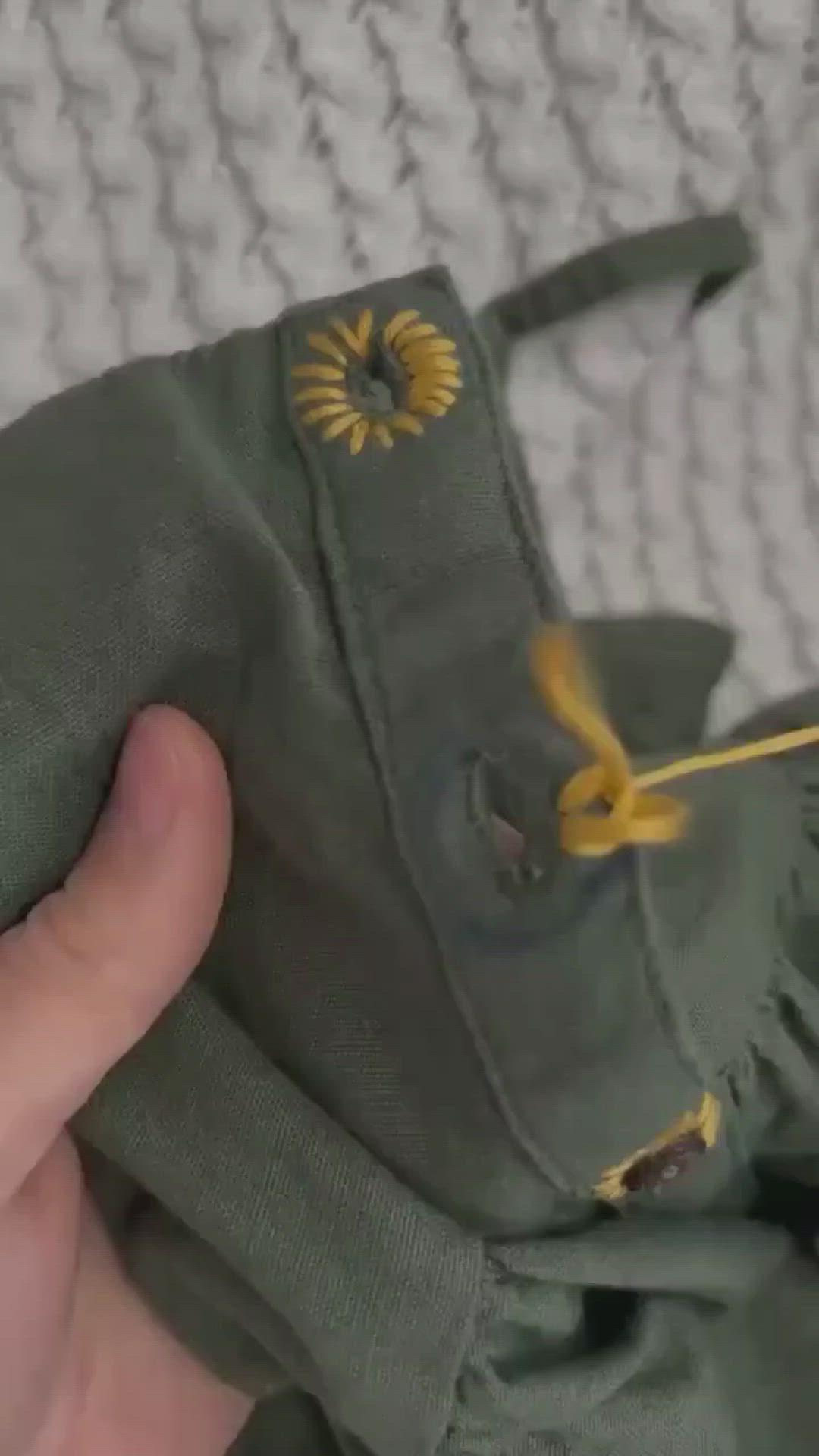 This may contain: a hand is holding an army green jacket with yellow flowers on the front and side