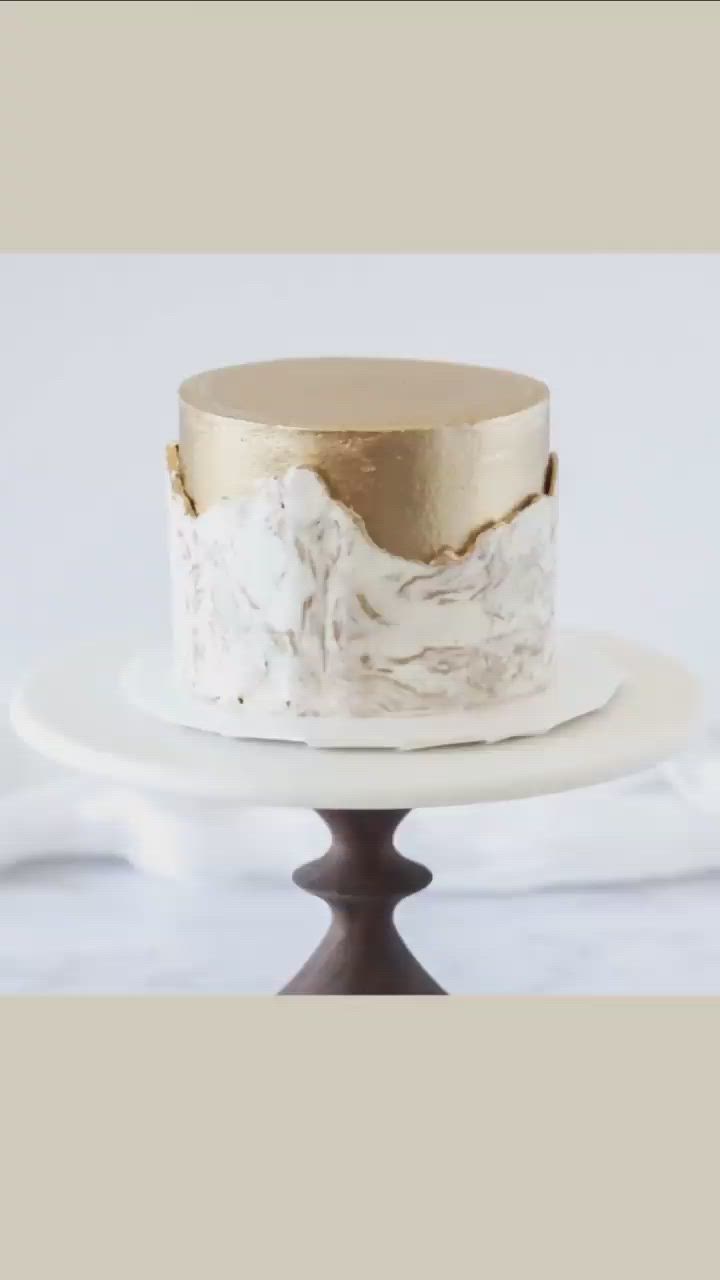 This may contain: a white and gold cake sitting on top of a plate