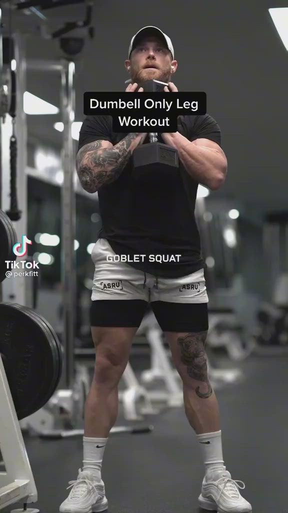 This may contain: a man squatting in the gym with dumbbells on his legs and holding a cell phone