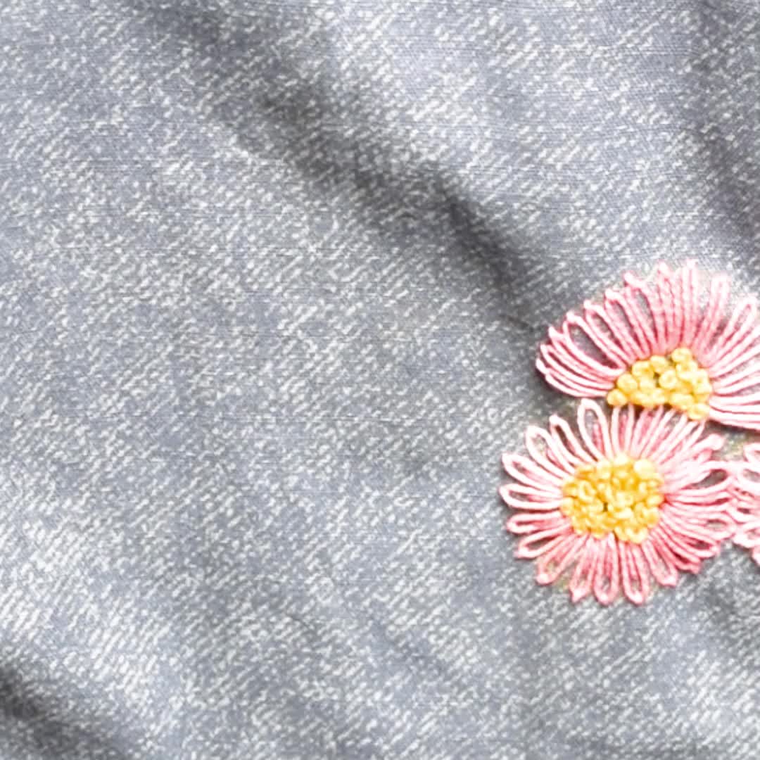 This may contain: three pink flowers with green leaves on a gray fabric background, in the middle of an embroidered design