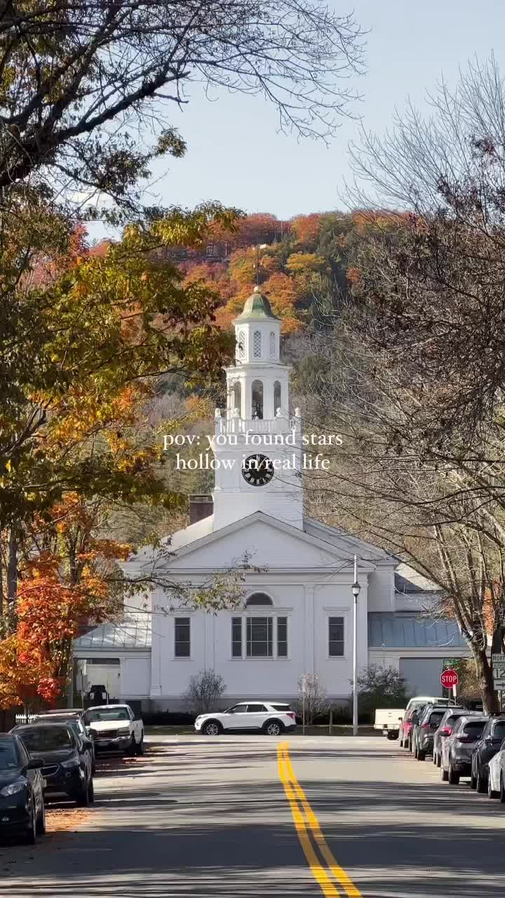This may contain: a white church with a steeple surrounded by trees and cars parked on the street