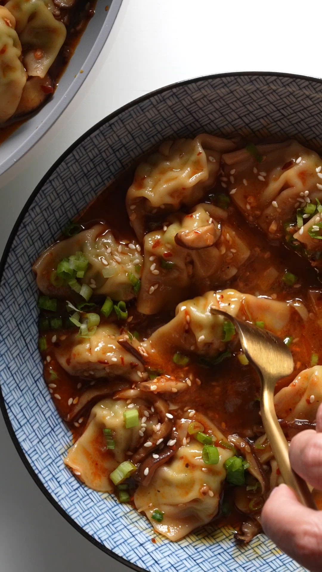 This contains: Making a chili sauce in a pan with mushrooms, and then adding chicken wontons to simmer. The wontons are added to a bowl and topped with sliced green onions,