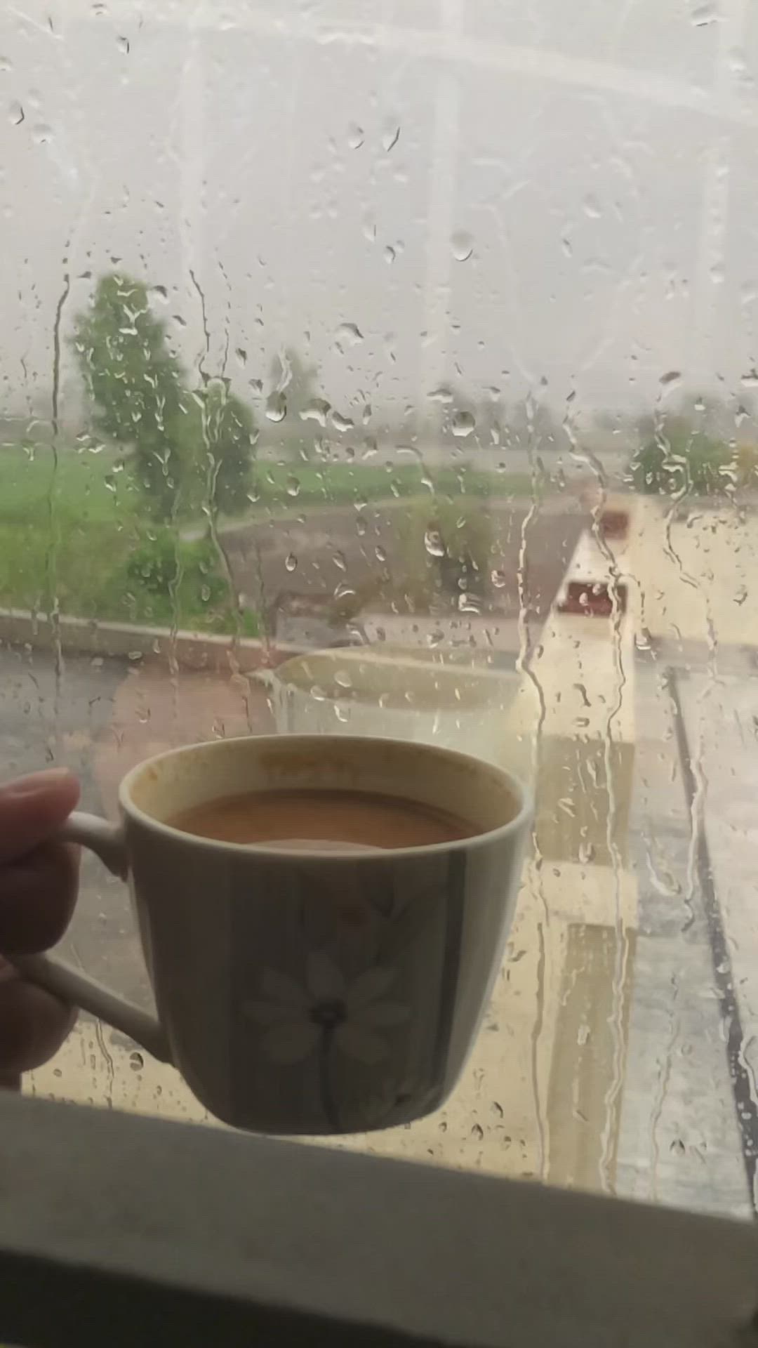 This may contain: a cup of coffee sitting on top of a window sill next to a rain soaked window