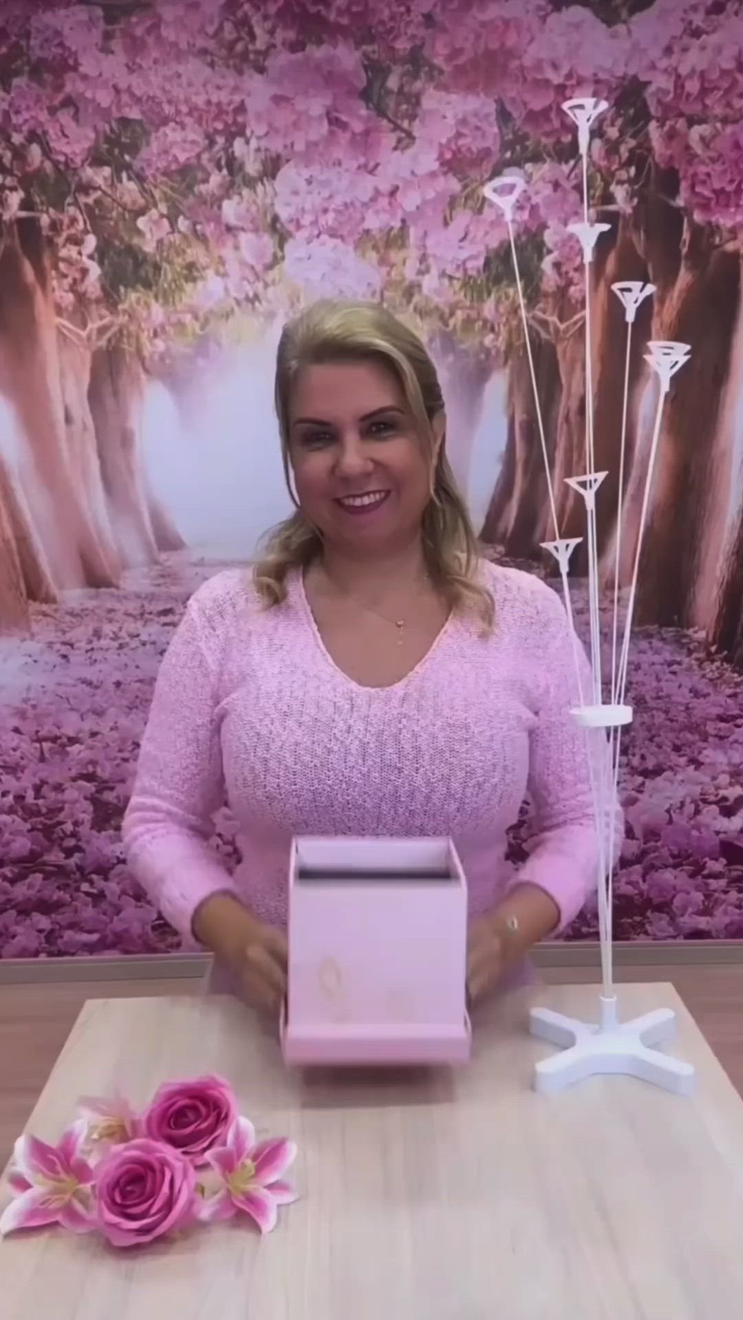 This may contain: a woman is holding a box with flowers in it and posing for the camera while sitting at a table