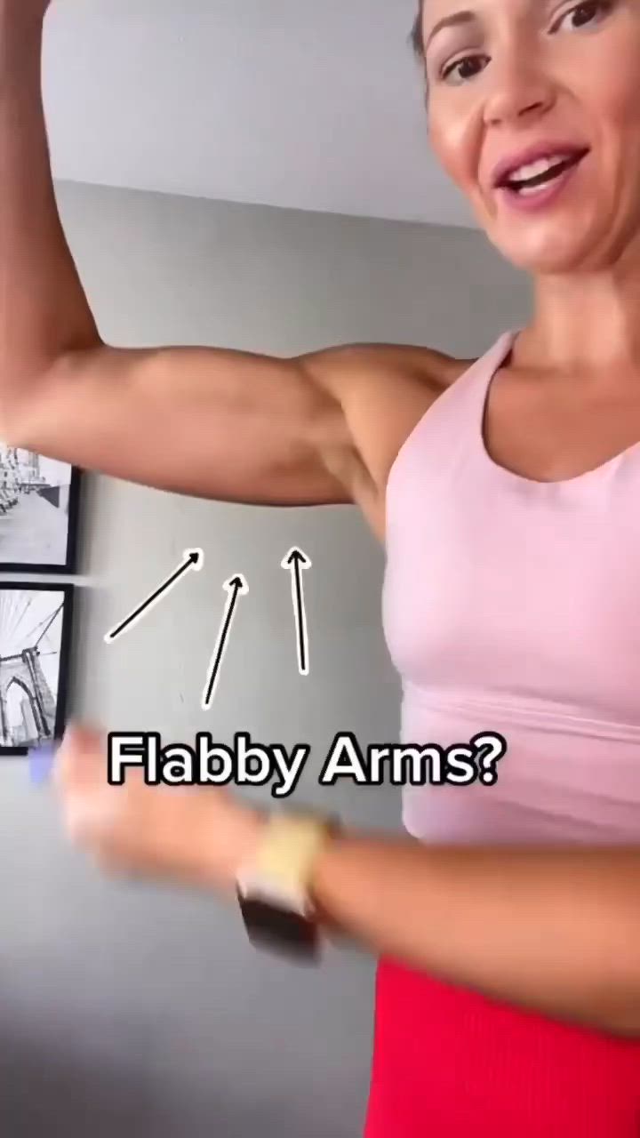 This may contain: a woman is flexing her arm muscles in the living room, with text that reads what do you think about flabby arms?