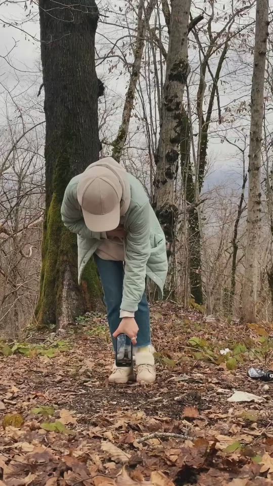 This may contain: a person bending over to pick up leaves from the ground in front of a tree