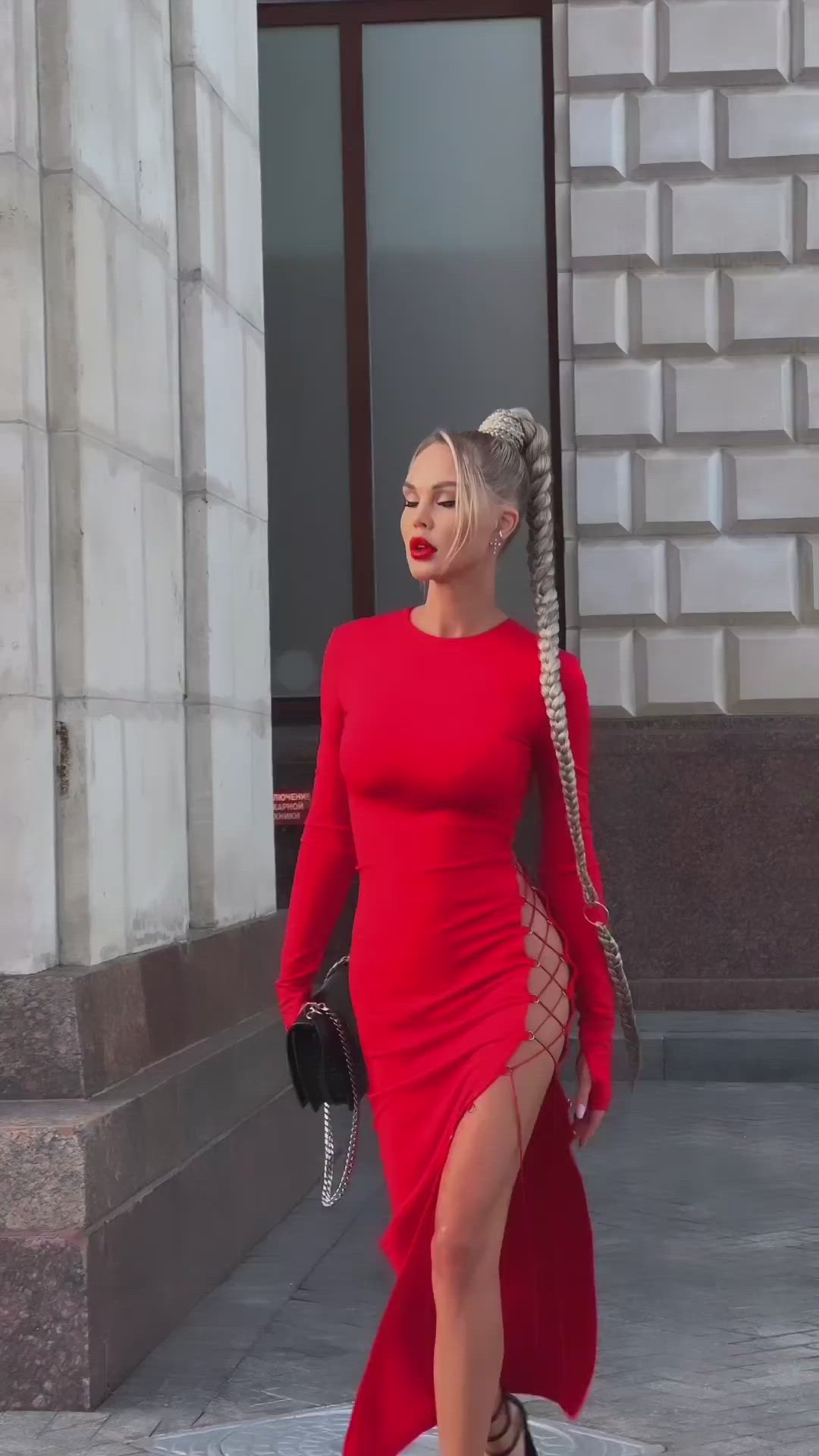 This may contain: a woman in a red dress with braids on her head is walking down the street