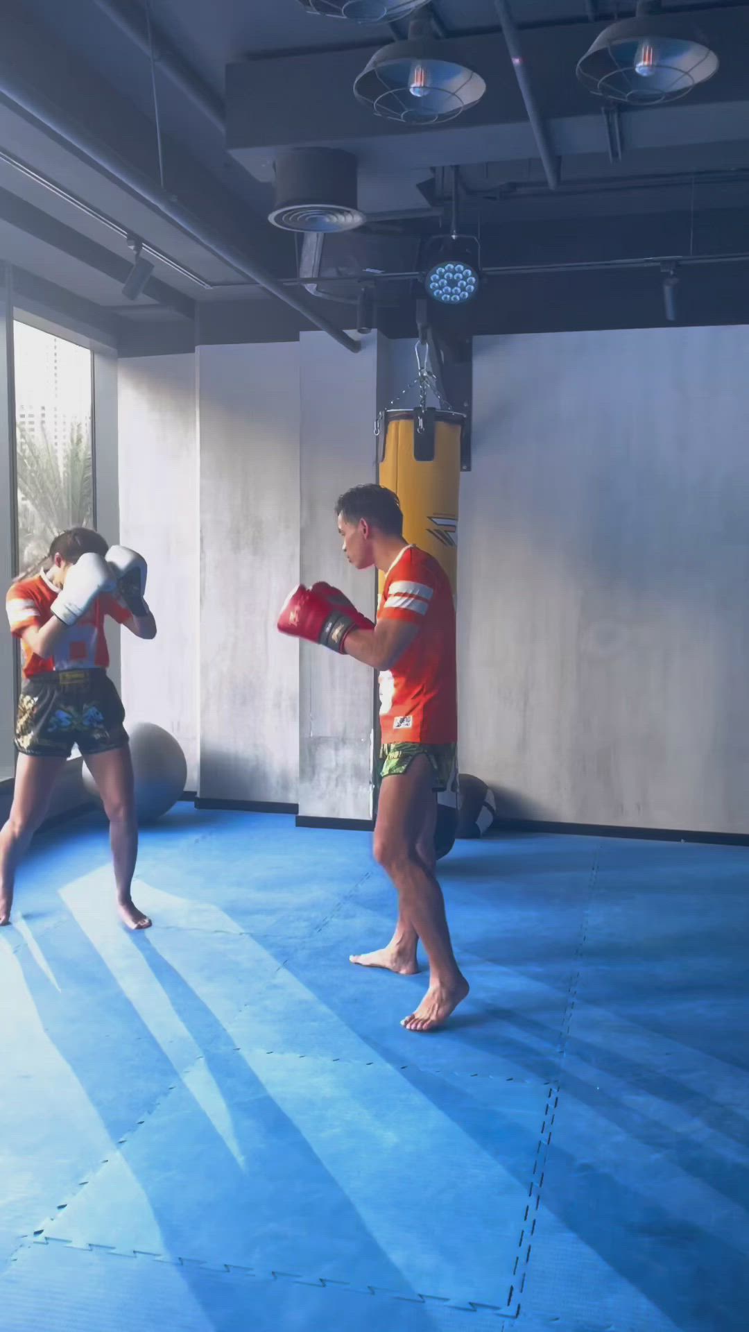 This may contain: two young men practicing boxing in an indoor gym area with blue flooring and white walls