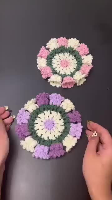 This may contain: two hands are holding crocheted flowers on a table with another person's hand