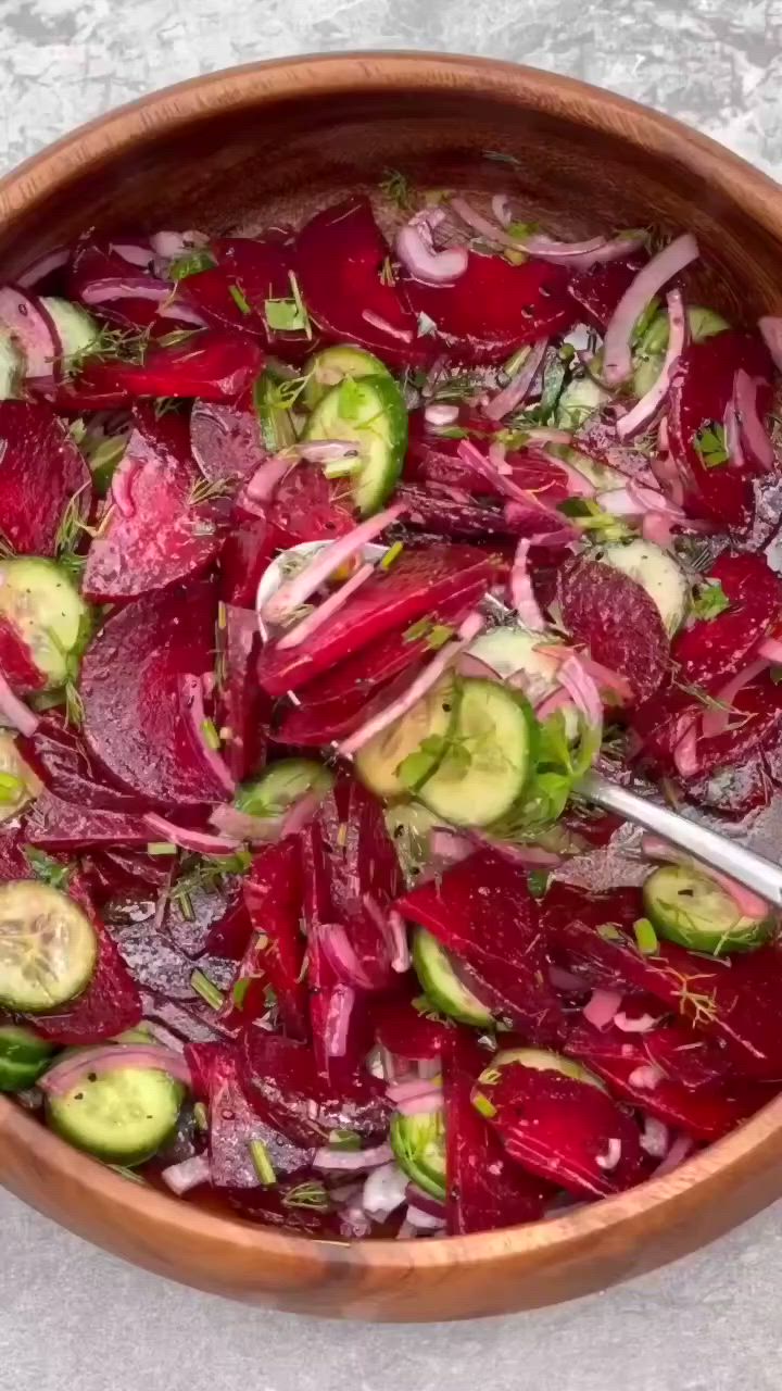 This may contain: a wooden bowl filled with beets and cucumbers on top of a table