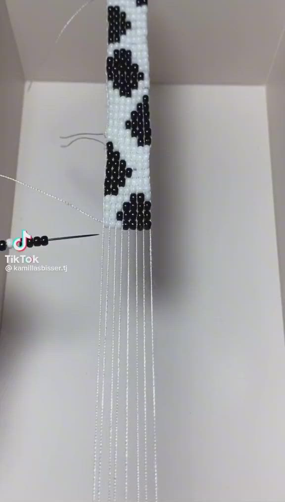 This may contain: a beaded sculpture in the shape of a tower with black and white beads hanging from it's sides