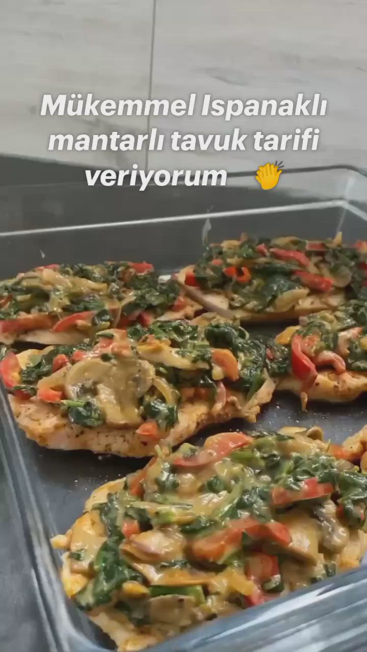 This may contain: chicken with spinach and red bell peppers in a glass dish on a counter top