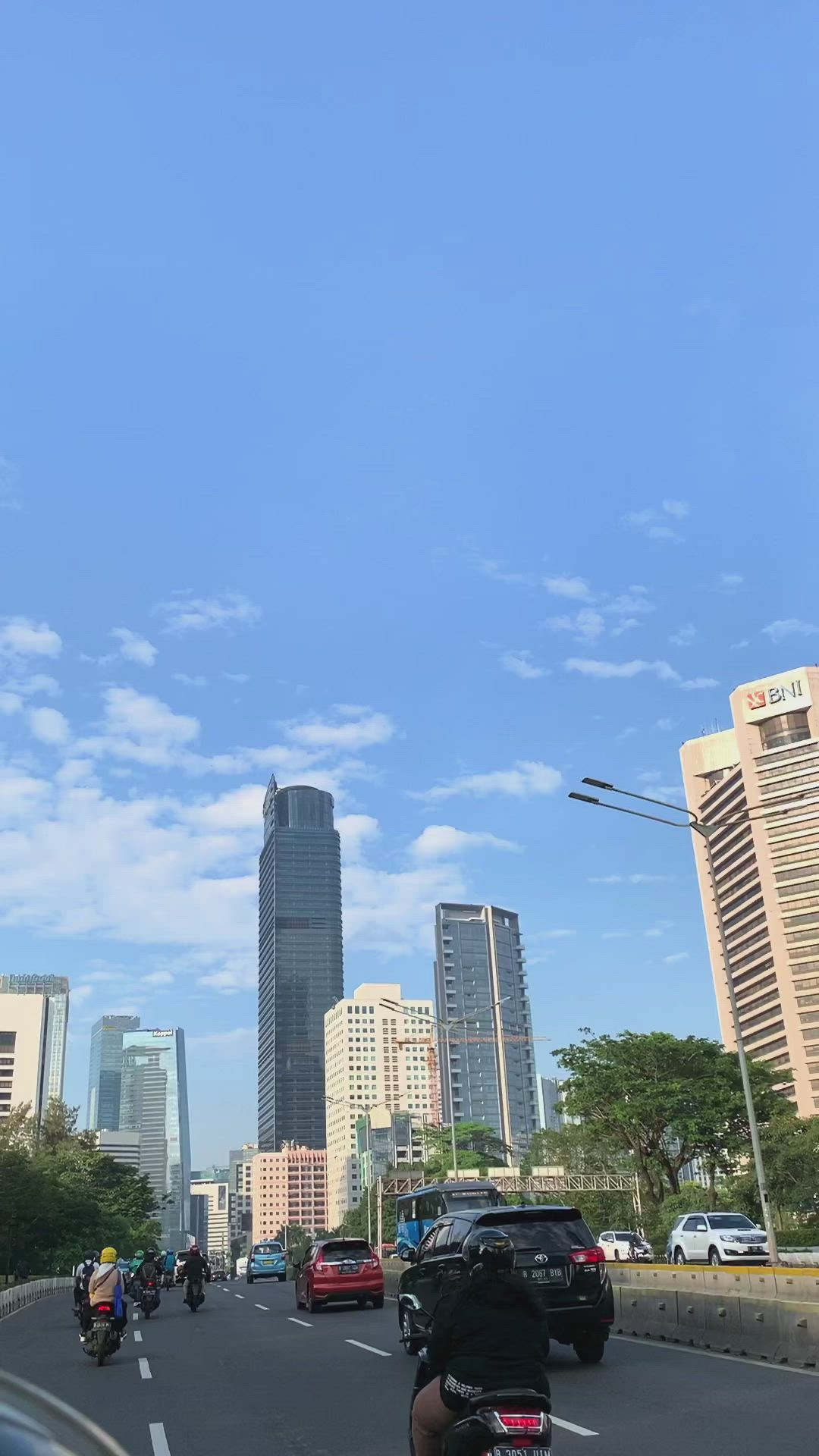 This may contain: people are riding motorcycles down the street in front of tall buildings and skyscrapers on a sunny day