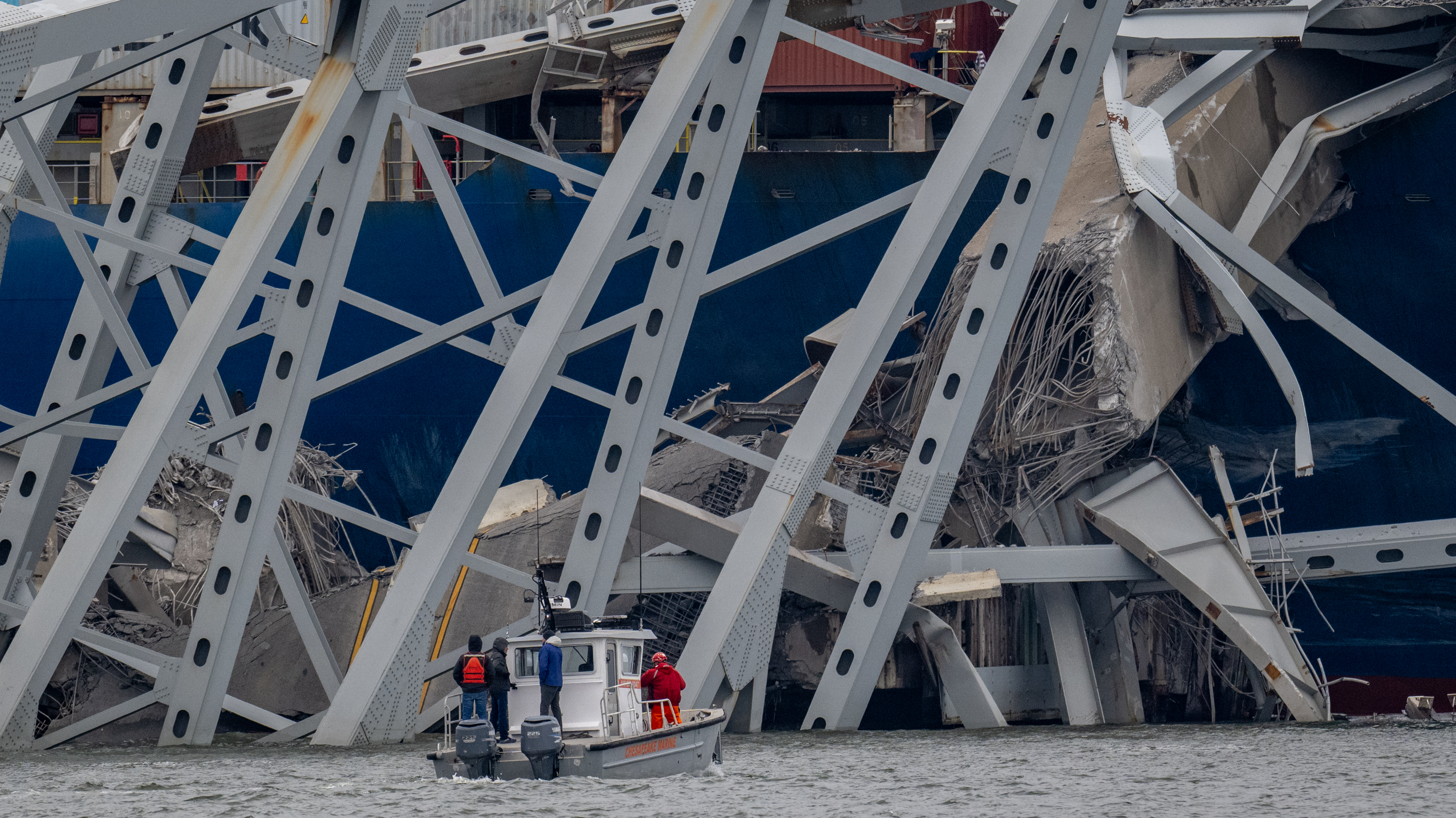 March 28, 2024: A work boat is dwarfed by the twisted structure from the Francis Scott Key Bridge draped across the container ship Dali. Early in the morning of March 26, the Dali lost power while leaving the Port of Baltimore and struck a support pier of the Key Bridge causing a catastrophic failure. (Jerry Jackson/Staff)