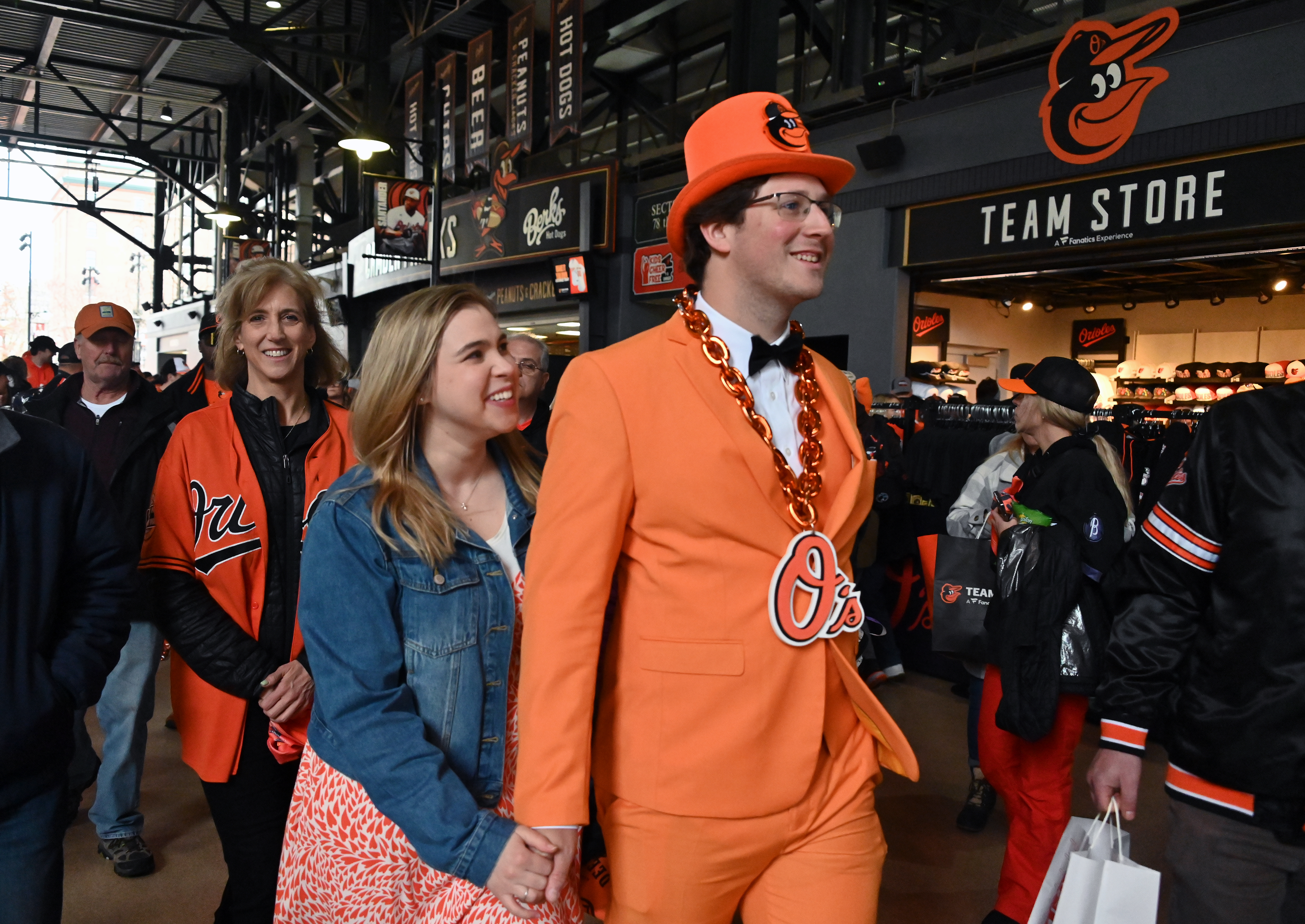 Mar. 28, 2024: Freddie Leatherbury, of Catonsville, walks with his girlfriend Rebecca Kazor, of Washington, DC, and his mother Theresa Leatherbury, of Towson, in the concourse of Oriole Park at Camden Yards on opening day. Freddie wore the orange suit for opening day last years and every important game since. The Baltimore Orioles host the Los Angeles Angels. (Kim Hairston/Staff)