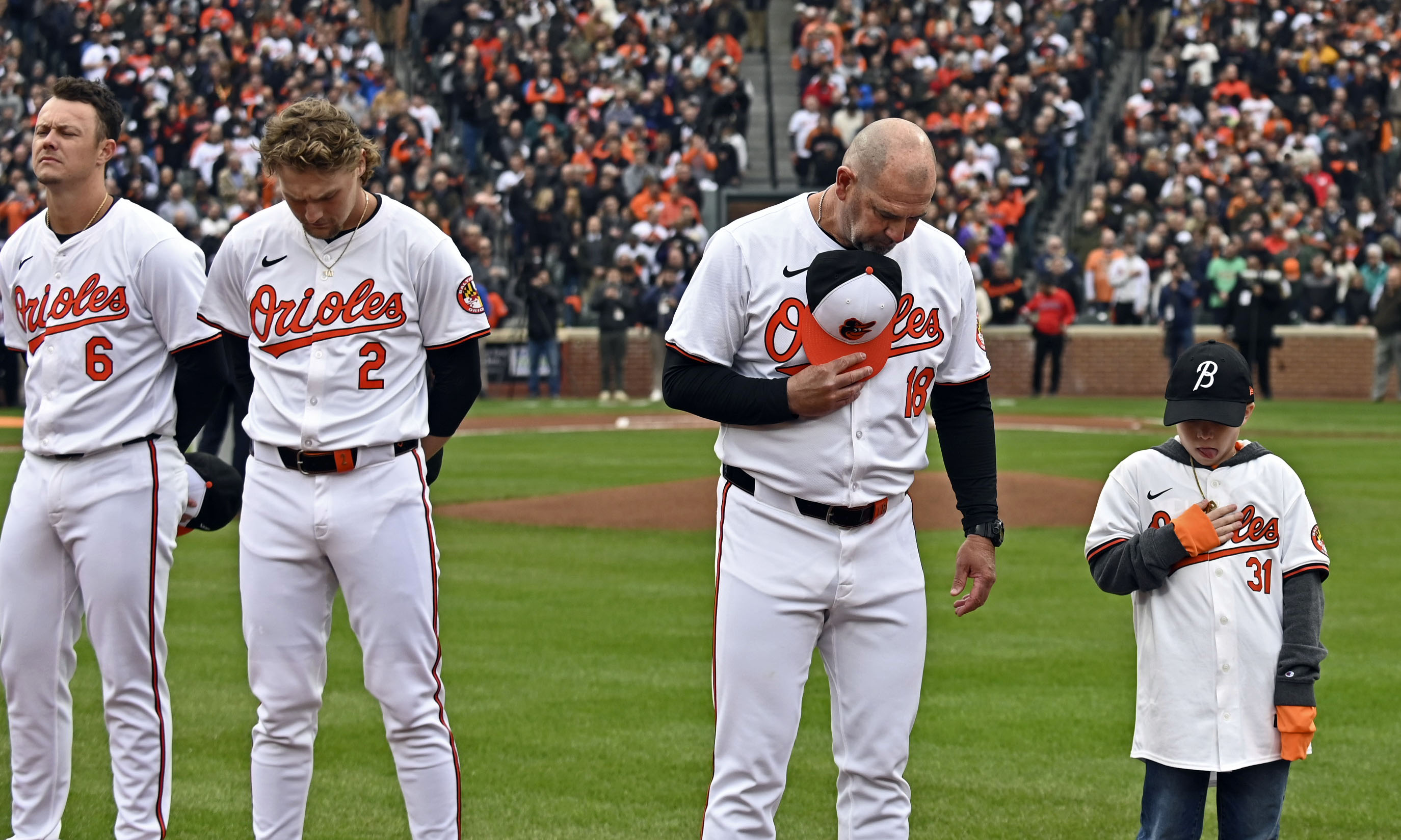 Mar 28, 2024: Orioles players Ryan Mountcastle, from left, Gunnar Henderson and manager Brandon Hyde with Carter, the Mo Gaba Fan of the Year, observe a moment of silent for the victims of the Key Bridge collapse at opening day. (Kenneth K. Lam/Staff)