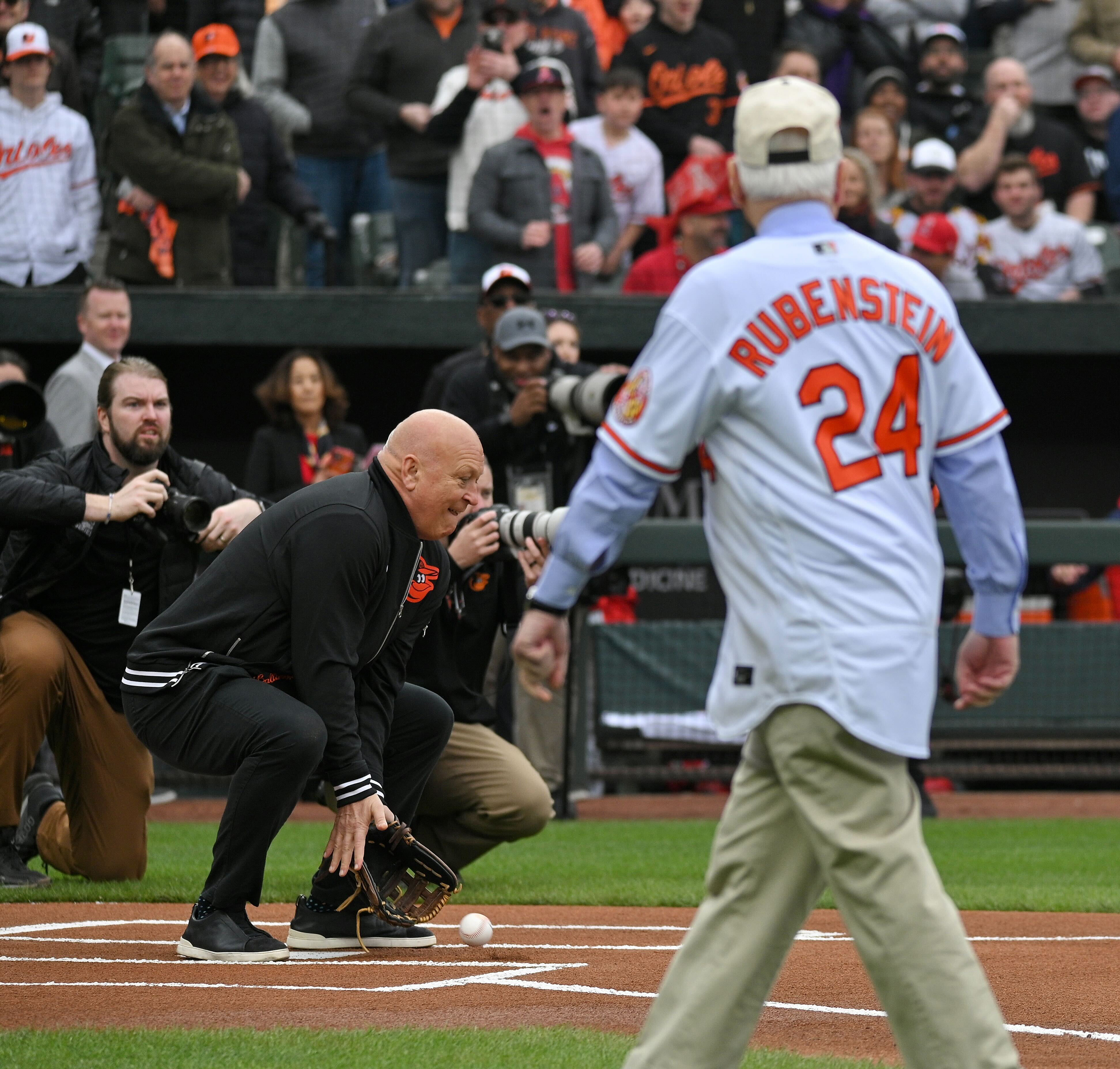 March 28, 2024: Former Orioles player Cal Ripken Jr. attempts to catch the ceremonial first pitch thrown by Aubree Singletary during opening day ceremonies at Oriole Park at Camden Yards. The new owner, David Rubenstein, watches the exchange. (Kenneth K. Lam/Staff)