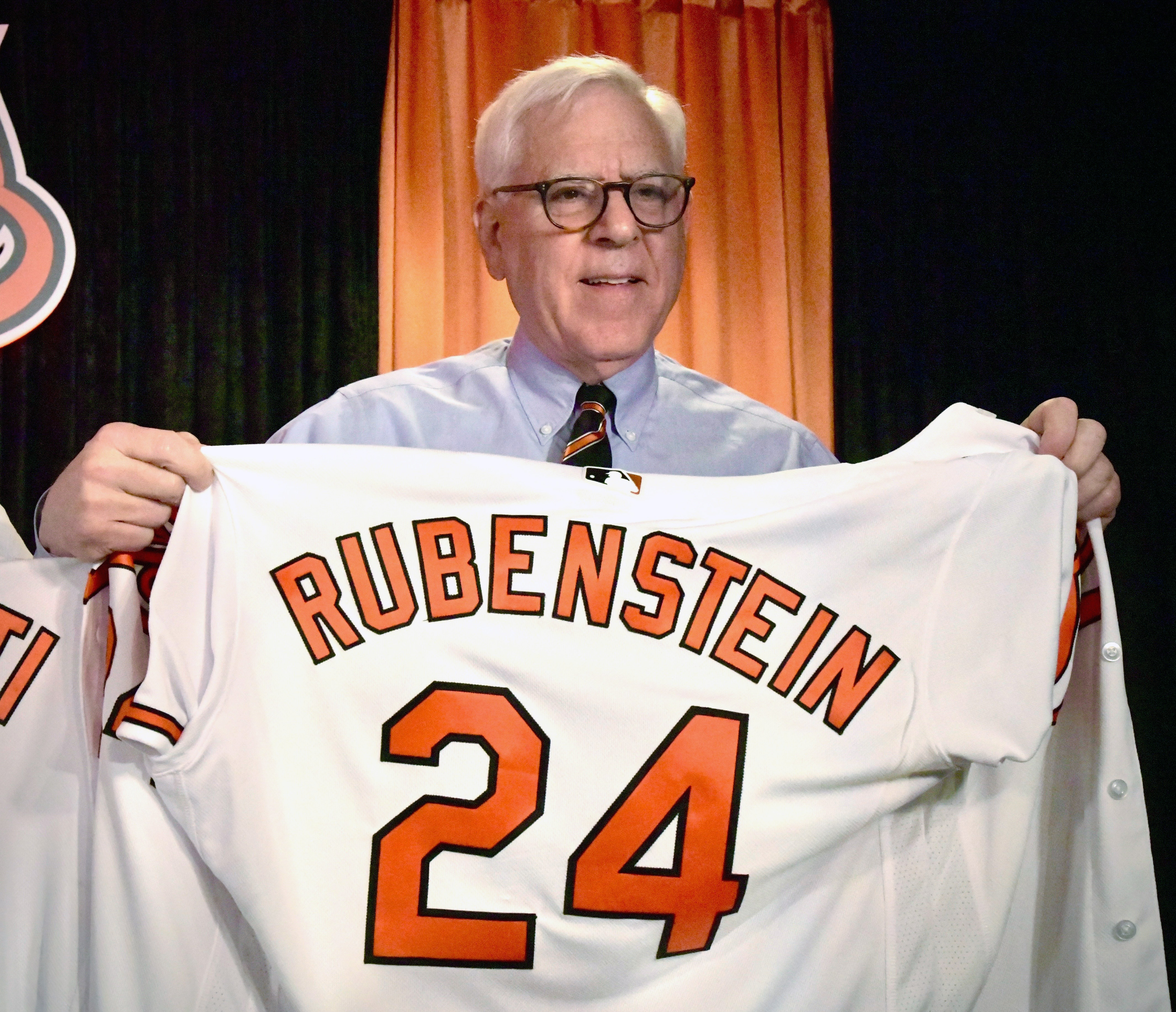 March 28, 2024: David Rubenstein, new owner of the Baltimore Orioles, shows off the Oriole jersey presented to him during a news conference on opening day. (Amy Davis/Staff)