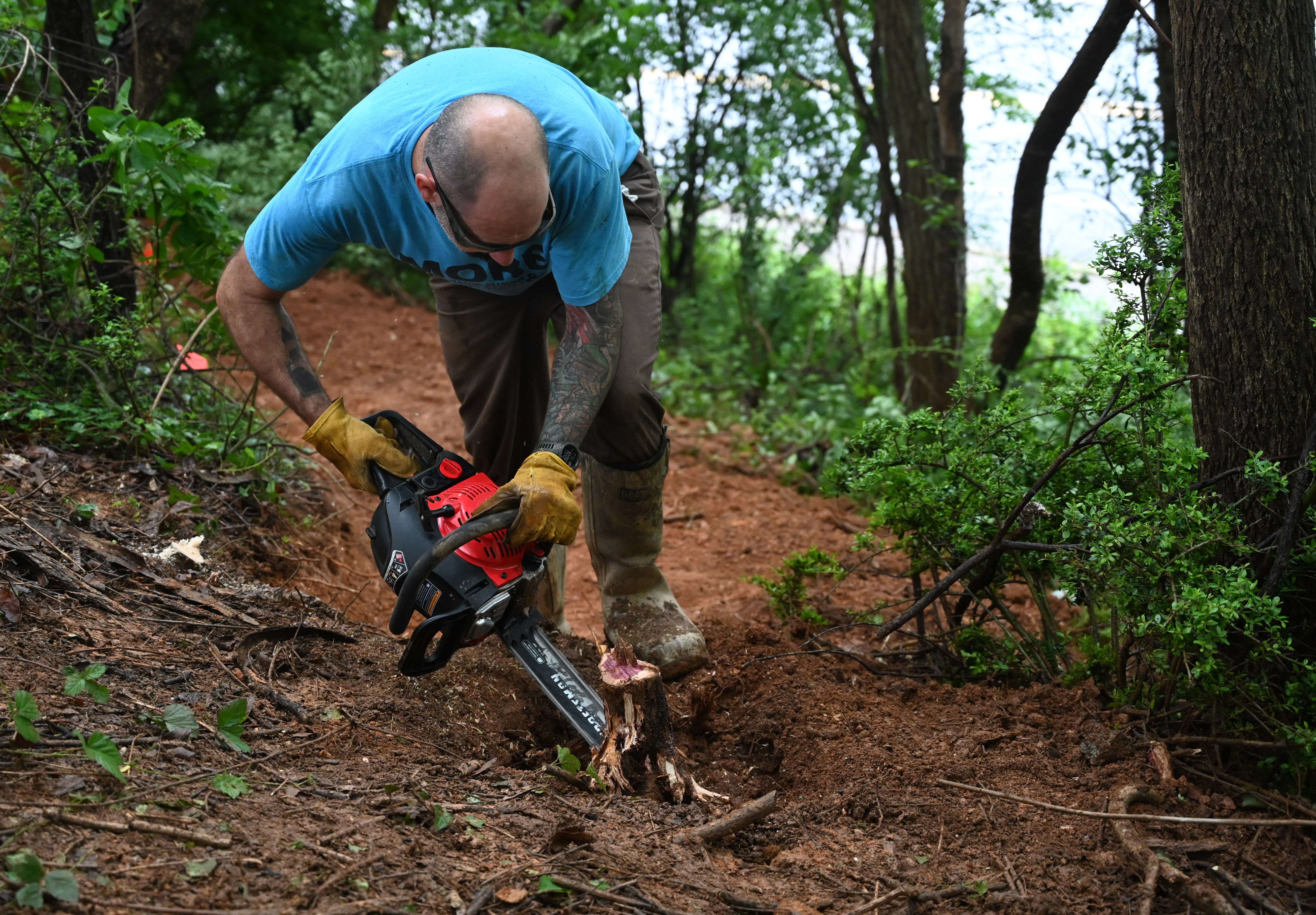 Dan Clark uses a chain saw to remove a stump from the middle of a path as a group of volunteers make progress in the creation of a new bike trail, Windy Ridge Trails, at Mount Airy's East West Park on Saturday. (Brian Krista/staff photo)