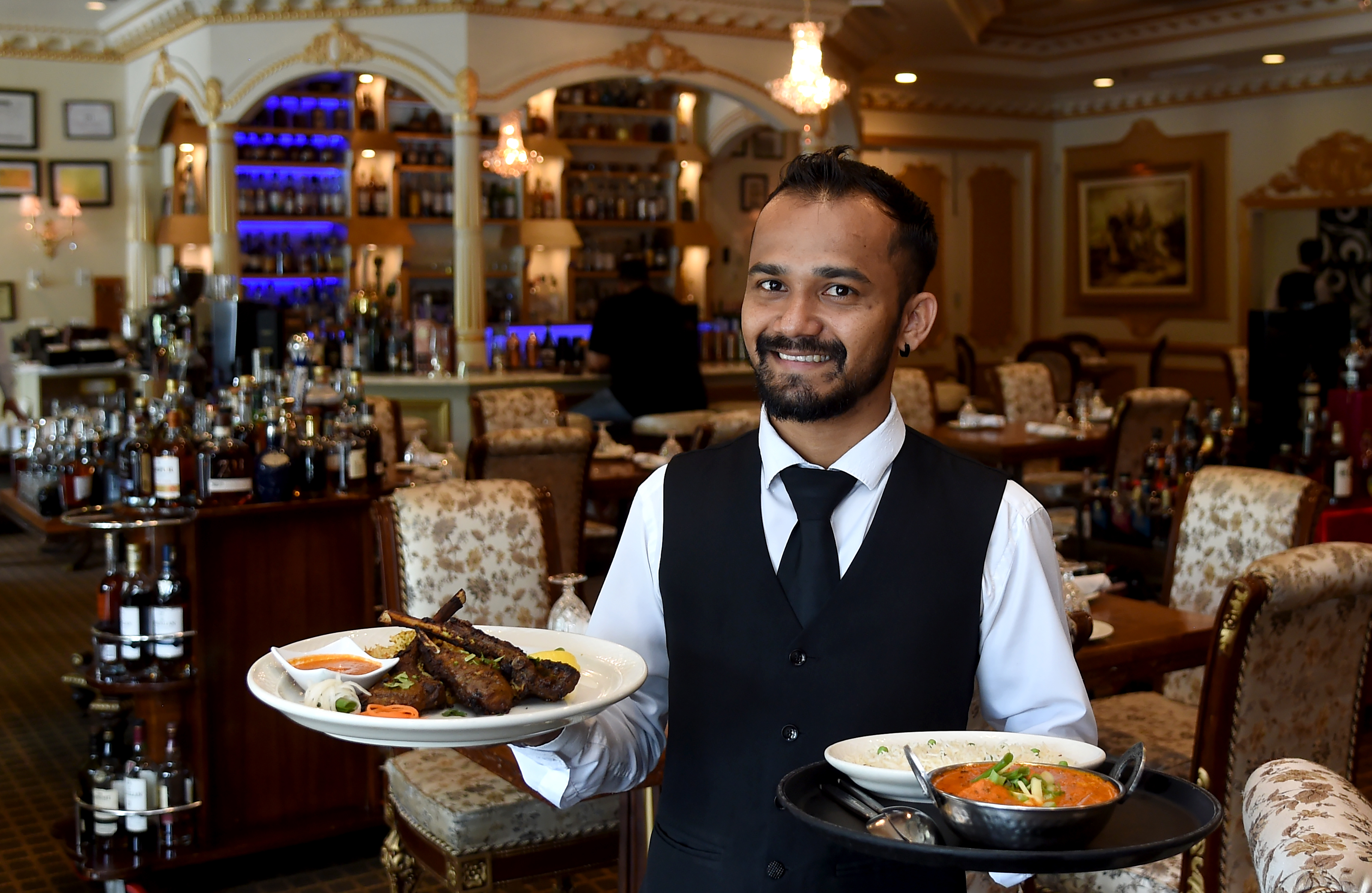 Alrich Pereira, a server and bartender at Royal Taj in Columbia, holds a platter of Tandoori Lamb Chops, left, and Chicken Tikka Masala, right, in the main dining room. Royal Taj was named best Indian restaurant in Howard County. (Barbara Haddock Taylor/Staff)