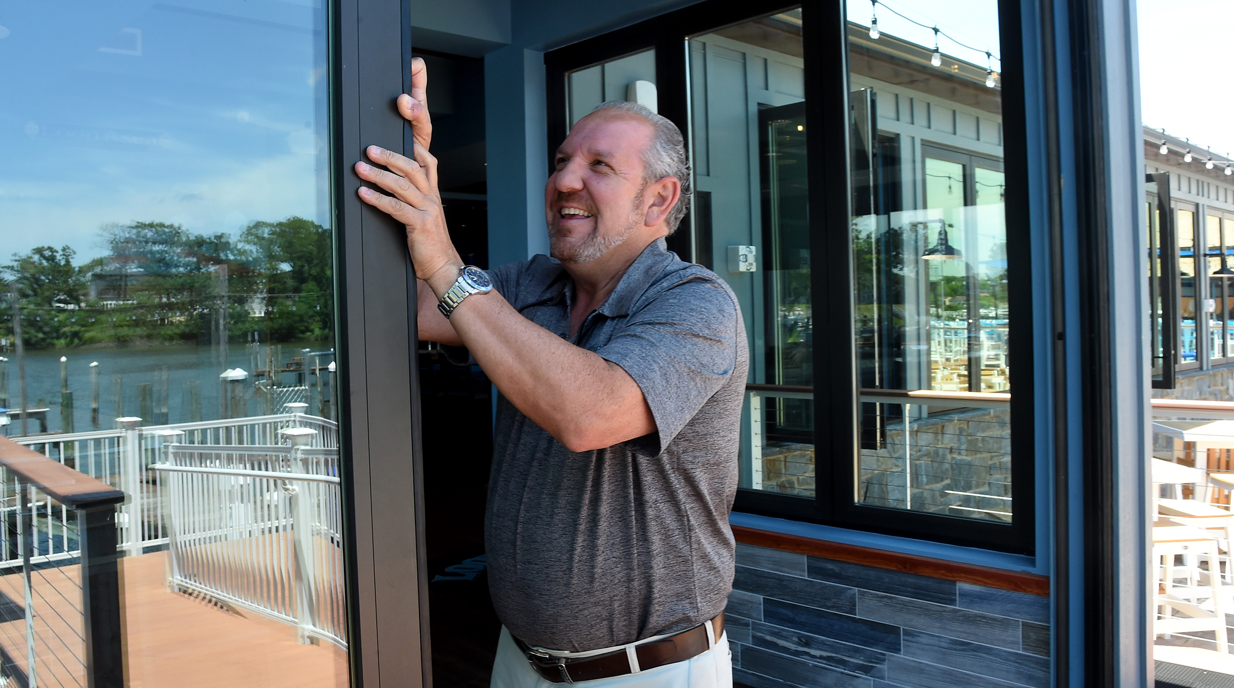 Co-owner Steven Litrenta opens one of the large windows, with the water reflected in it, at LoonAsea, his new waterfront restaurant/bar on Hopkins Creek in Essex. (Barbara Haddock Taylor/Staff)