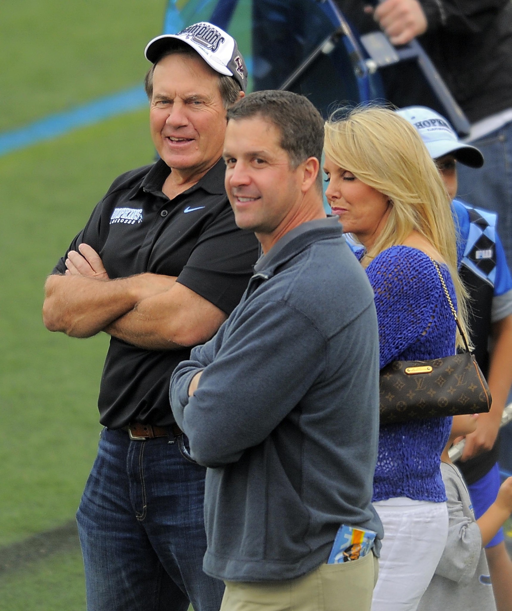 Baltimore Ravens head coach John Harbaugh (front) chats with New England Patriots head coach Bill Belichick and Linda Holliday at the Maryland-Johns Hopkins game.