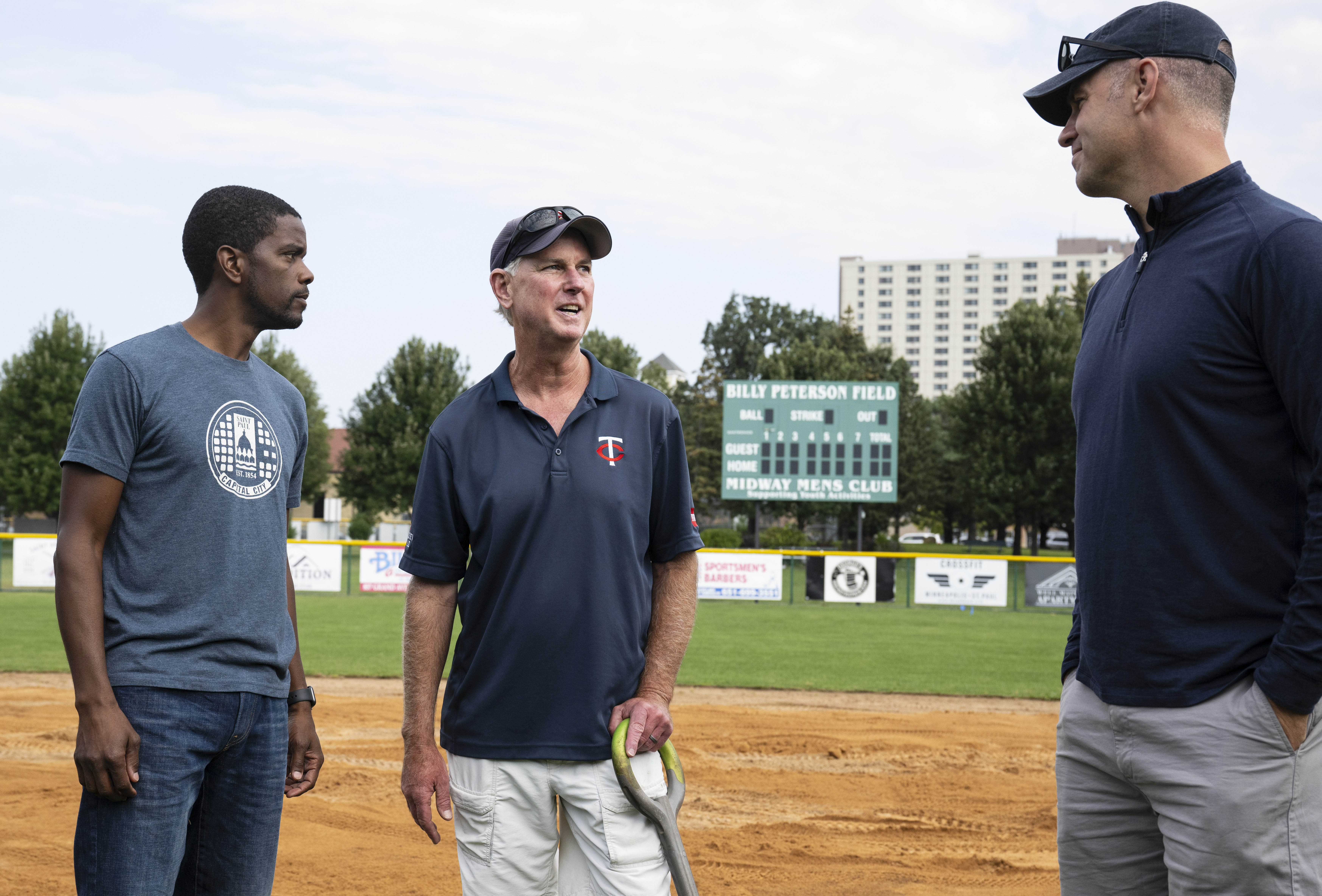 Three men talk on a baseball diamond.