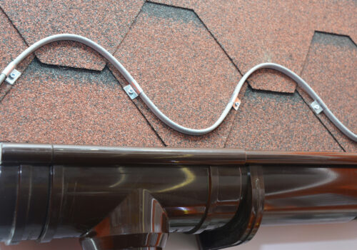 Roofing heating cable for ice and snow melting. A close-up on a roofing deicing system, ice-melting cable installed above the rain gutter on an asphalt shingled roof.