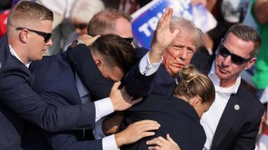 Donald Trump surrounded by Secret Service agents after being shot in the ear