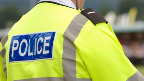 A police officer in a high-vis jacket with "police" on the back