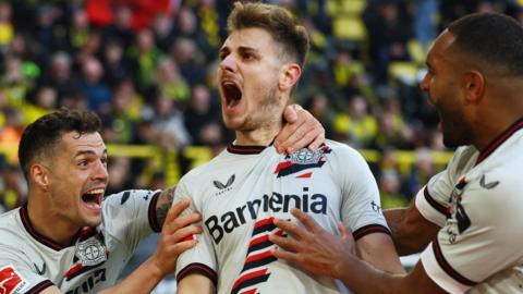 Josip Stanisic celebrates scoring a goal at Borussia Dortmund with Bayer Leverkusen team-mates Granit Xhaka and Jonathan Tah