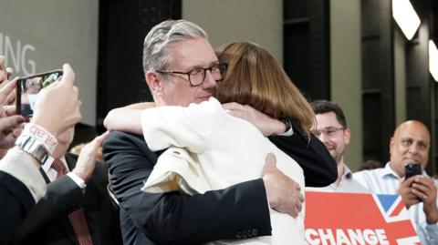 Labour leader Sir Keir Starmer embraces his wife Victoria at a watch party at Tate Modern surrounded by people looking happy