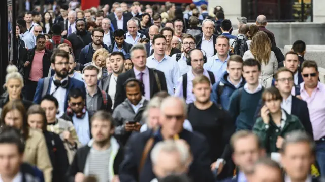 A crowd of commuters, mainly wearing suits, walk along a street