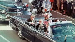 O presidente JFK desfila em carro aberto pouco antes de ser assassinado em Dallas, Texas, em 1963 