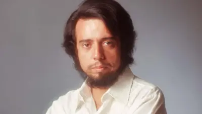 Sergio Mendes quando jovem, usando barba e camisa branca, e olhando para a câmera