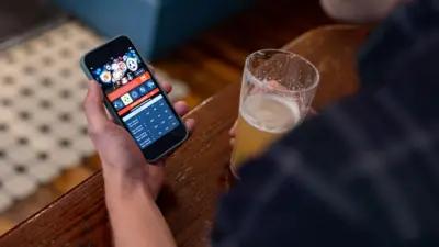 Homem tomando cerveja e fazendo apostas online em celular