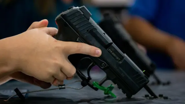 Uma mão de criança segura uma arma na Convenção da National Rifle Association