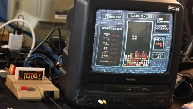 Aparelho Nintendo com cartucho de Tetris inserido e Tetris num monitor de TV