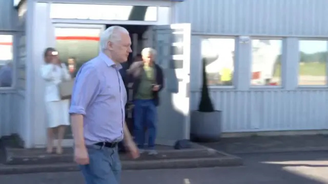 Assange caminhando em pista de aeroporto
